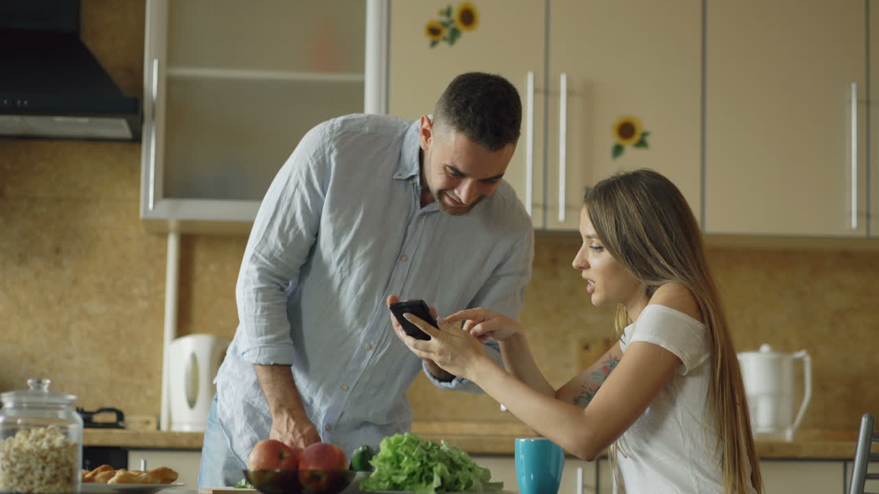 Couple preparing a meal together in the kitchen, looking at a recipe on a smartphone.