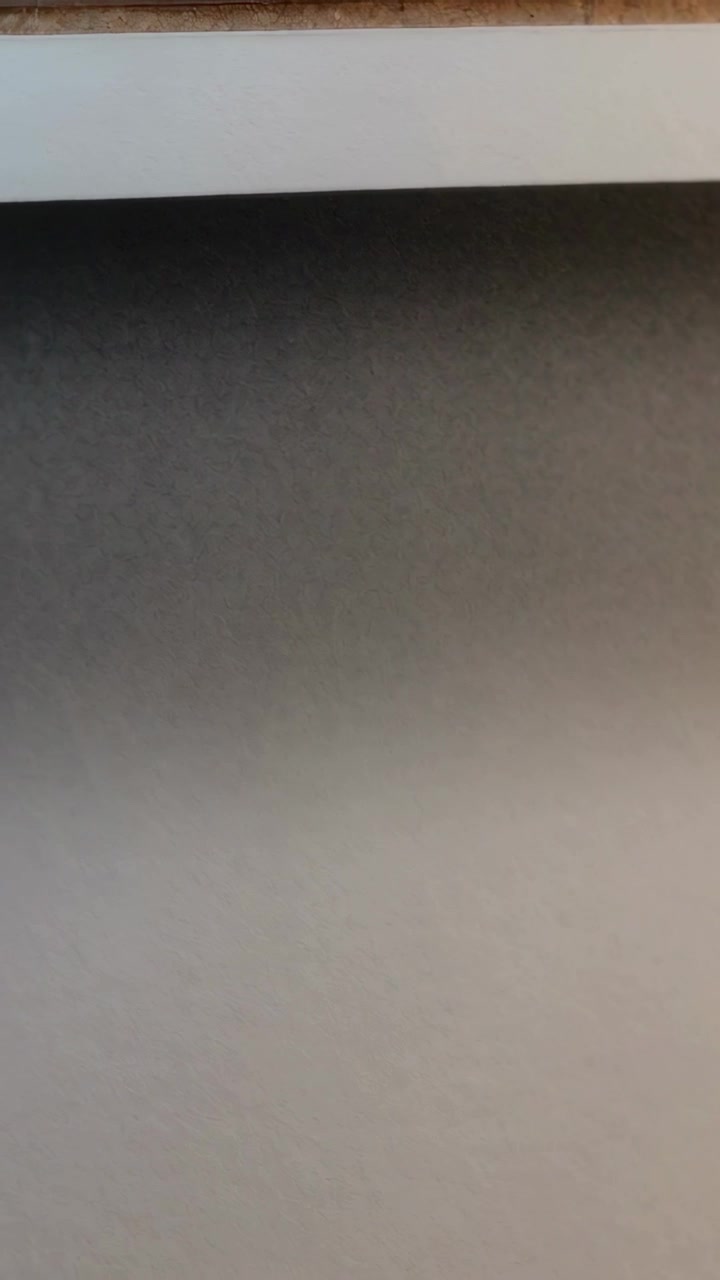 Verticale video: Bewegende camera filmt een geschilderde muur met wit lijstwerk en een lichte schaduw in de kamer.
