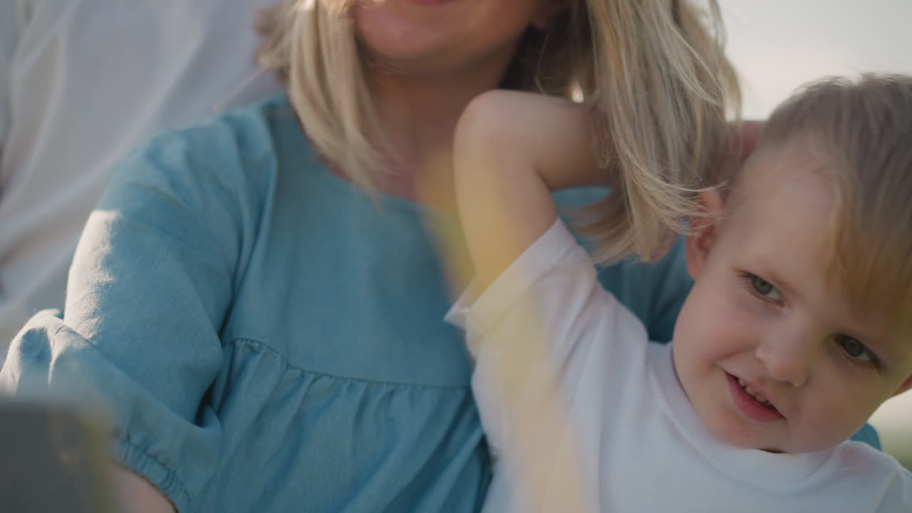 Close-up of a little boy wearing a white shirt, sitting comfortably on his mother s lap. The mother s face is partially visible, with a warm smile, creating a tender moment between them