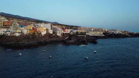 amazing drone shot in 4k at tenerife in spain los gigantes at the coast seashore seaside with boats and mountains in the background city buildings hotels sea blue water lagune