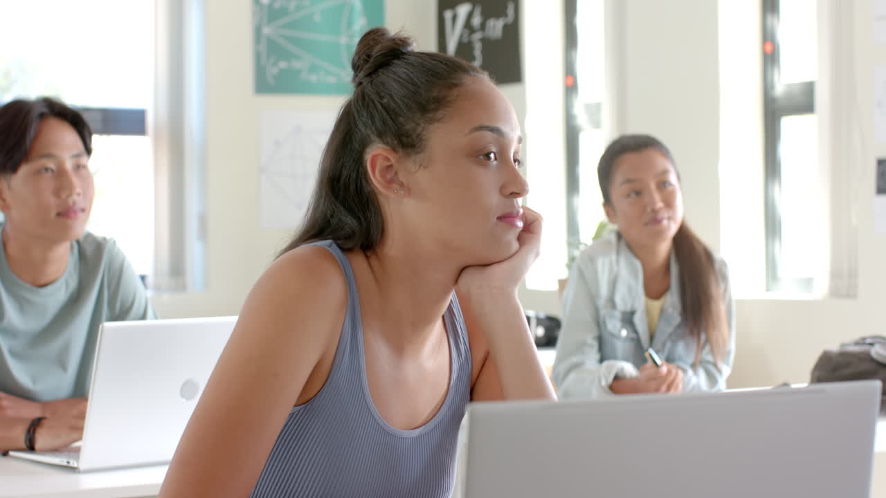 In high school, teenage girl sitting at desk with laptop, looking bored