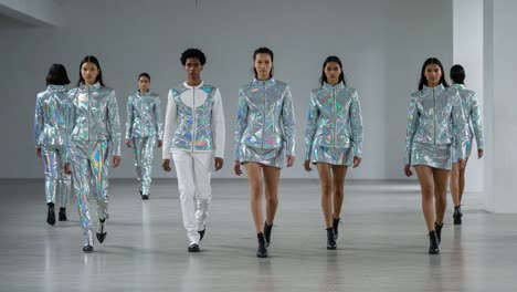 a striking fashion showcase: models walk the runway in futuristic, reflective outfits with sleek designs and unique silhouettes, capturing modern trends in innovative style