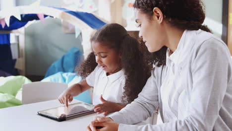 Young-black-schoolgirl-using-a-tablet-computer-and-learning-one-on-one-with-female-teacher,-close-up