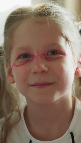 chica de escuela con cara pintada sonríe sentada cerca de la pizarra en un fondo borroso. el hermano menor estira los labios de la hermana con los dedos haciendo una sonrisa más amplia de primer plano