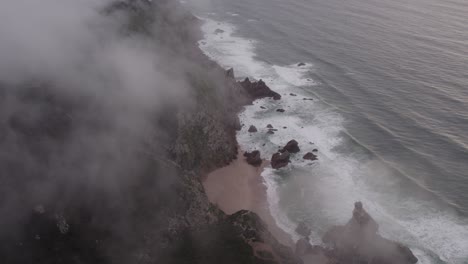 aerial view of praia da ursa portugal with low clouds above the sea, drone shot