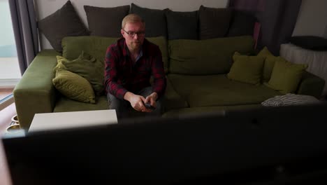 el hombre caucásico con barba se sienta en el sofá, usa el control remoto, el día informal en casa