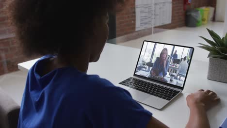 Back-view-of-african-american-woman-having-a-video-call-on-laptop-with-female-colleague-at-office