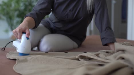 woman uses a machine for removing pellet and spools from clothes and fabric on black trousers. a modern electronic device for updating old things