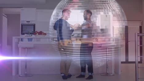 Animation-of-disco-ball-and-light-trails-over-diverse-male-couple-dancing-in-kitchen