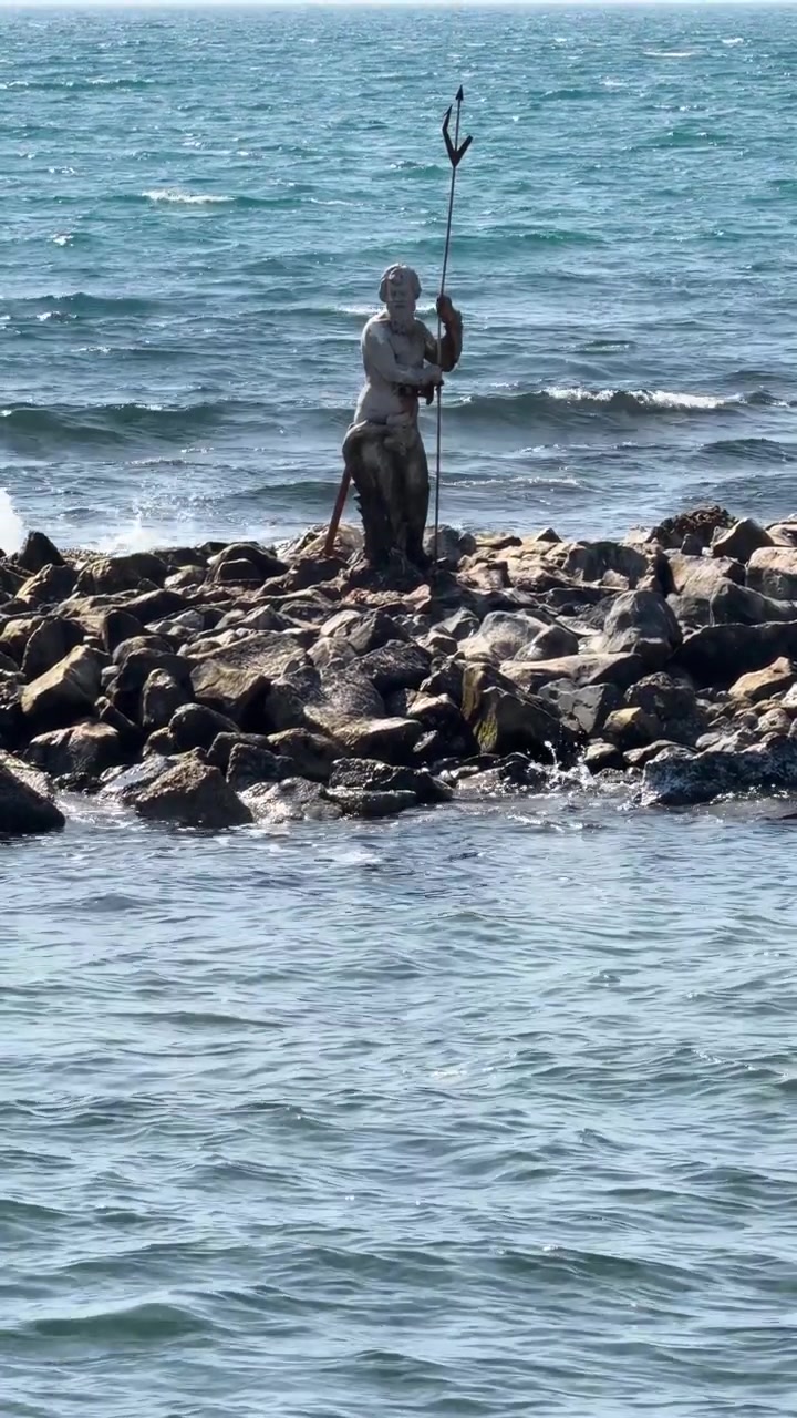 Statue of god Neptune with his trident on rocky reef in middle of sea in Ostia