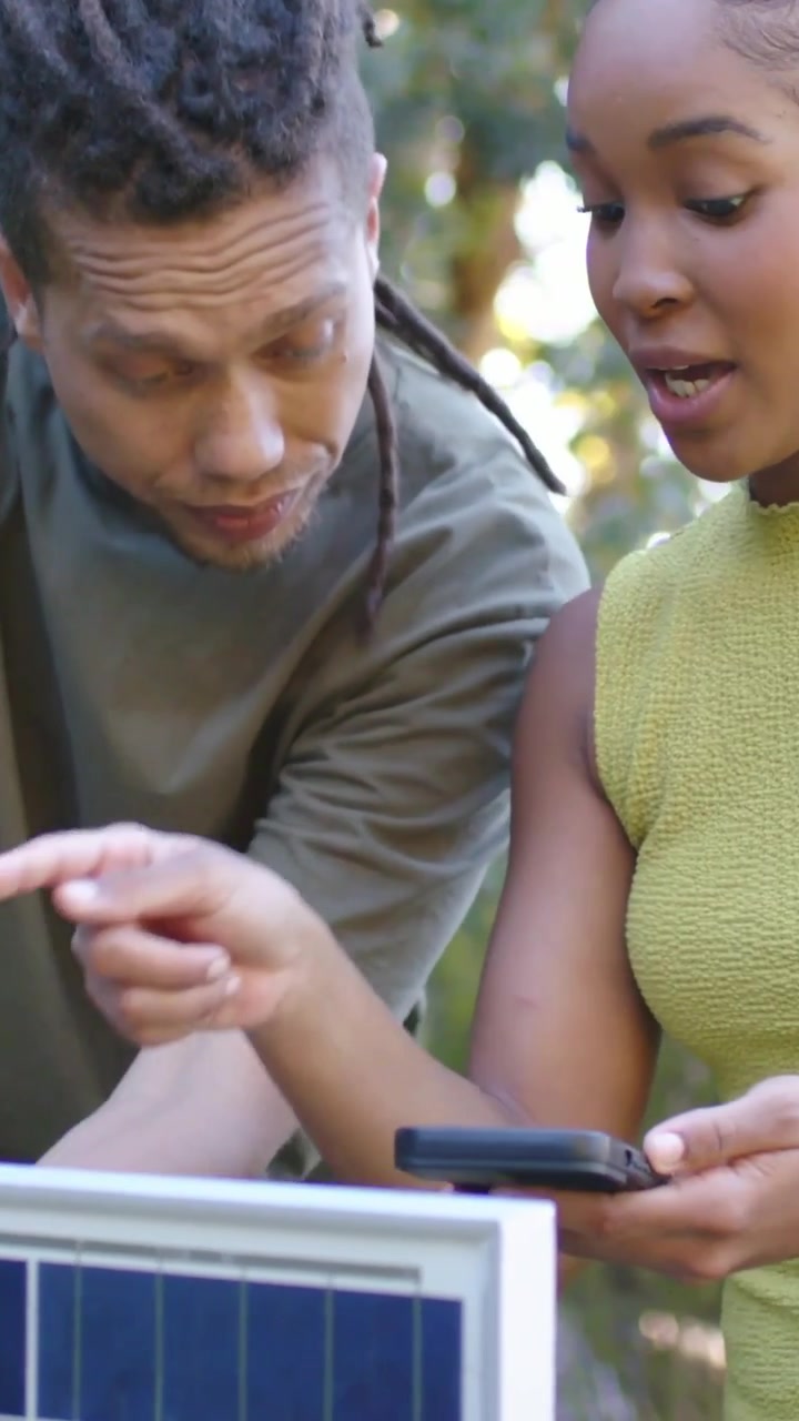Vertical video: Leaning man checking panel in yard, woman joining in green showing phone to confirm