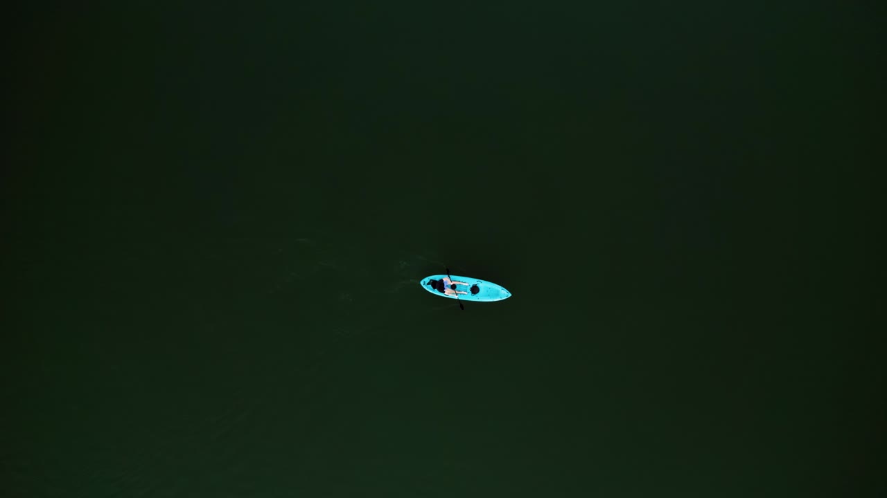 Arial view of solo kayaker on dark water, peaceful and serene mood