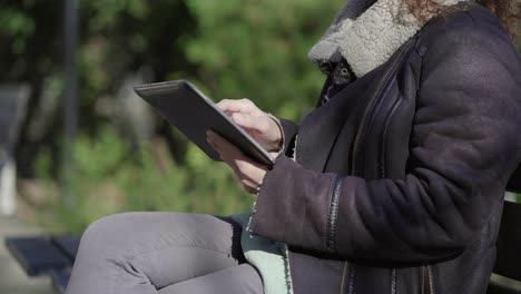 Captura-Recortada-De-Una-Mujer-Vestida-Con-Ropa-Abrigada-Usando-Una-Tableta-Al-Aire-Libre