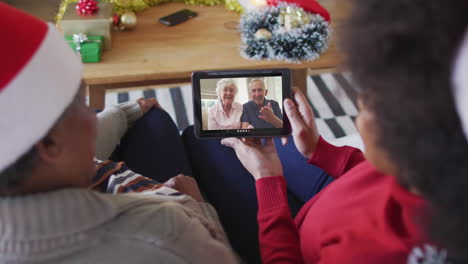 madre y hija afroamericanas usando una tableta para una videollamada de navidad con una pareja en la pantalla