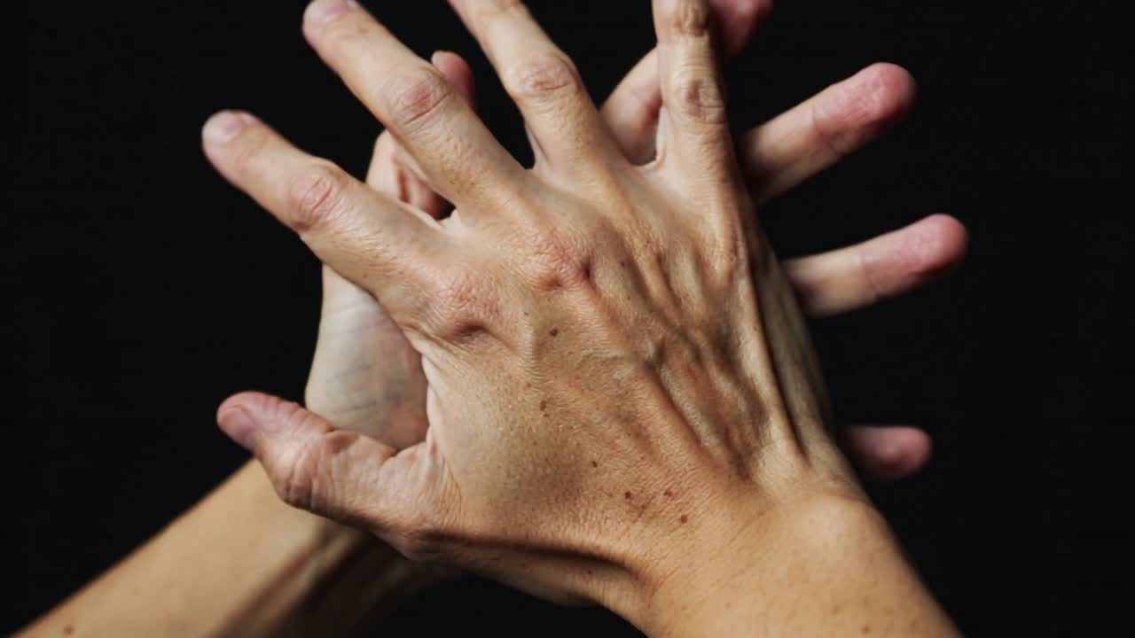 Manos envejecidas presionando y extendiéndose, moviéndose y girando sobre un fondo negro que muestra la textura de la piel.