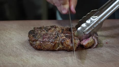 closeup of succulent steak: knife cutting on cutting board holding it with clippers