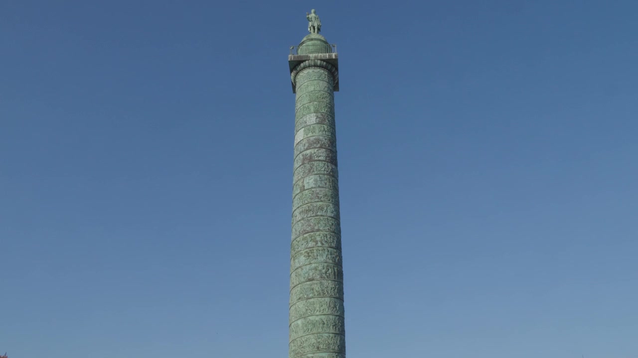 Tilt-up shot of the Vendome Column at Place Vendome in Paris, showing the bronze Napoleonic monument and statue rising against a clear blue sky.