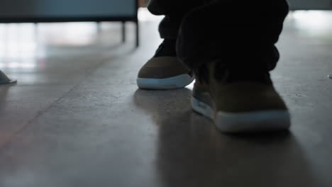 Close up of legs in dark trousers walking slowly on polished marble floor, wearing stylish sneakers with white soles and black laces, creating a calm and confident movement under soft indoor lighting