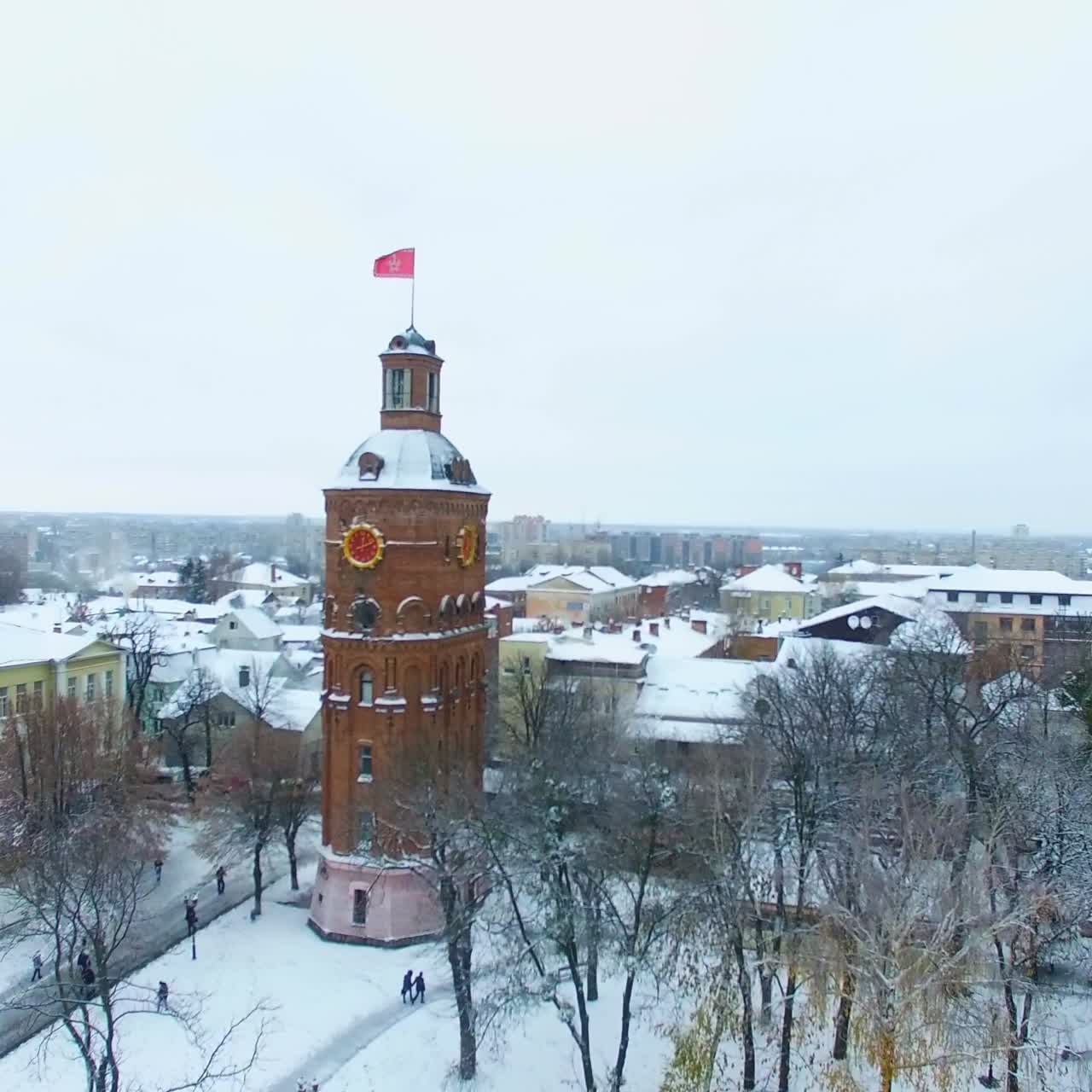 Square with old water tower in the centre of Vinnytsia, Ukraine. Drone ascending over the snowy trees and historic buildings. Aerial view