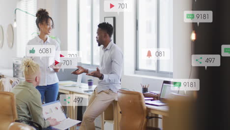 anmation of social media icons falling against diverse colleagues discussing together at office