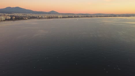 POV-of-Birds-Flying-over-the-water-at-sunset,-Birds-Eye-View,-Flying-Home,-Seagulls-nesting,-Thessaloniki-Greece,-Waterfront-at-sunset,-White-Tower-of-Thessaloniki