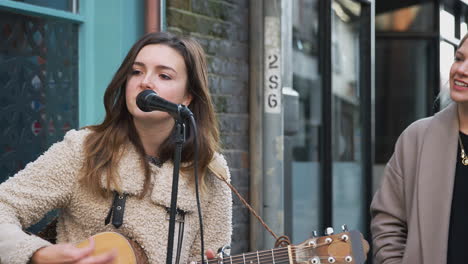 female musician busking playing acoustic guitar and singing to crowd outdoors in street