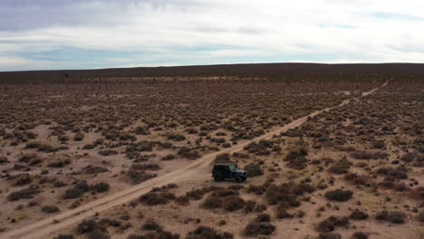 orbiting aerial view of a jeep parked in the middle of the mojave desert wilderness - man walks into the rugged terrain