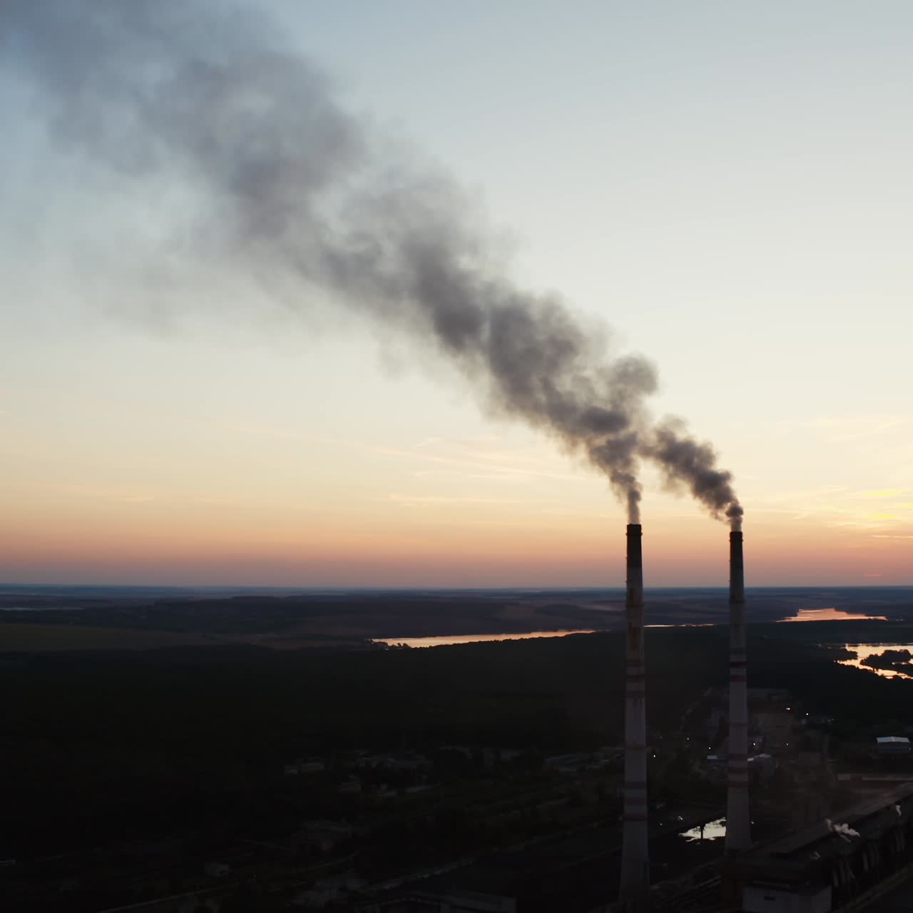 Ecological disaster. Dirty emissions from industrial pipes on the natural environment in the evening. Factory near the river at sunset.