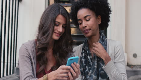 two beautiful woman friends sitting on steps having fun talking selfie on smart phone