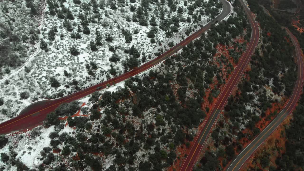 Aerial pan up shot following a car on a winding road separating the snow covered red rock mountains of Zion national park.