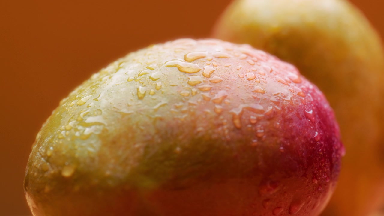 Mango con gocce d'acqua in rotazione su sfondo arancione.