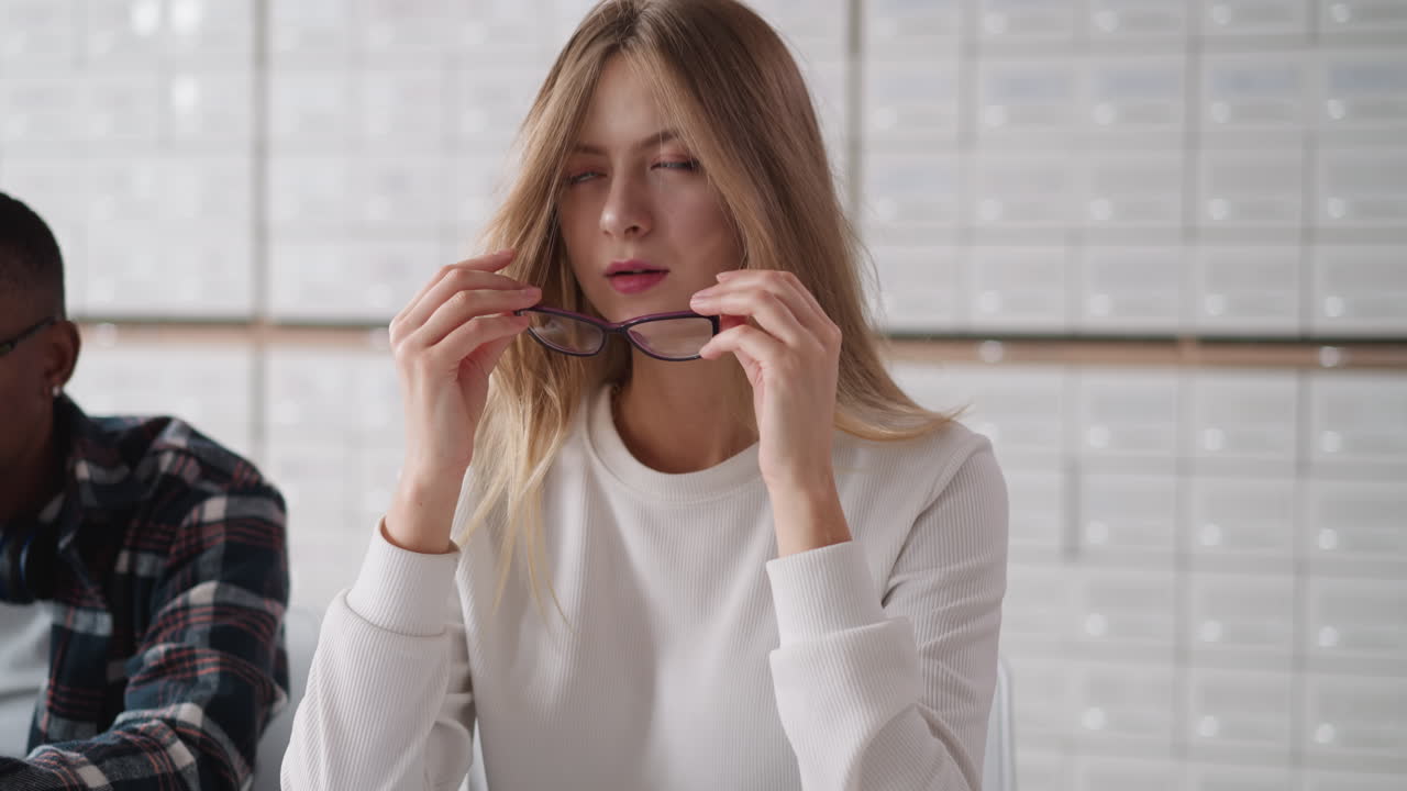 Woman takes off glasses against card index case. Blonde lady adjusts long loose hair sitting at desk in university library. Student tired to learn
