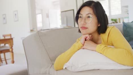 Glückliche-Asiatische-Frau,-Die-Auf-Der-Couch-Im-Wohnzimmer-Liegt