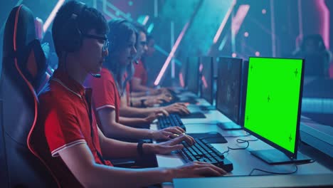 Professional Gamer Plays in a Video Game with Mock-up Green Screen Display on a Championship. Team of Pro Gamers in Stylish Neon Cyber Games Arena. Online Broadcasting of Tournament. Side View