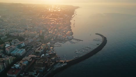 A stunning aerial view of an Italian harbour town at sunrise, with sunlit coastal houses and a tranquil harbour, capturing the serene beauty of the Mediterranean coastline in the early morning light.