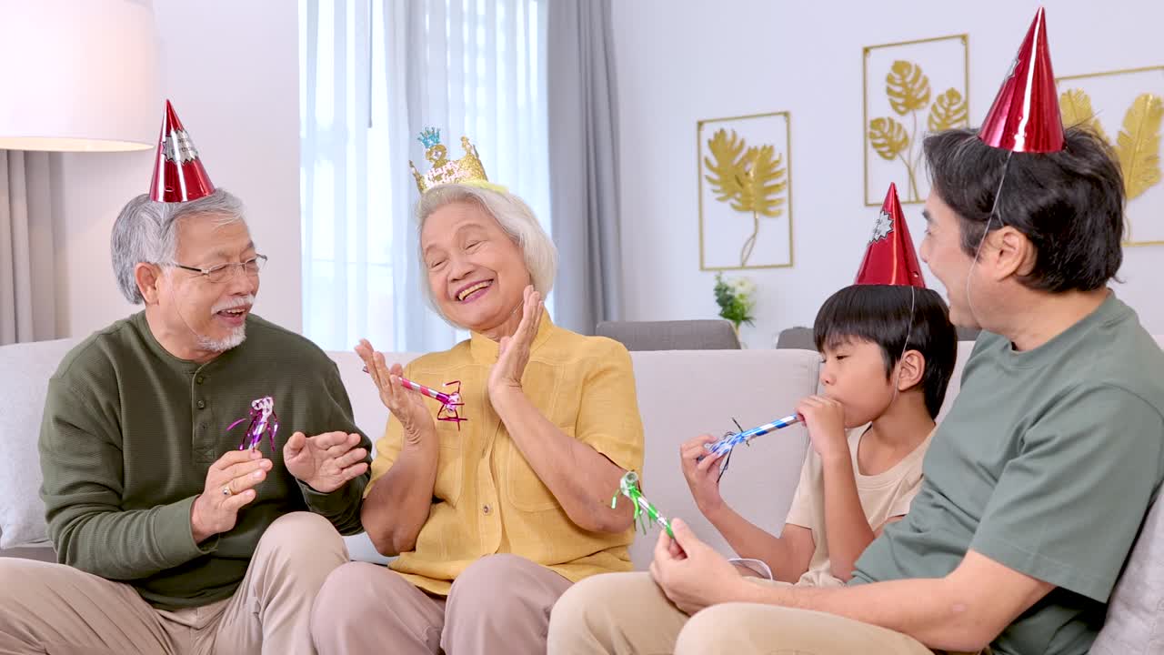 Three generations celebrate a birthday with party hats and noisemakers in a bright living room
