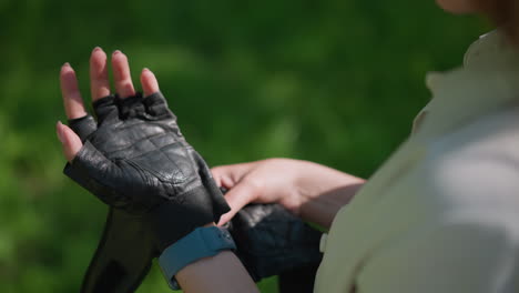 primer plano de la mano del individuo desabrochando la correa del guante de motociclista contra el telón de fondo de la vegetación exuberante, la mano está ajustando delicadamente el guante con enfoque en los dedos