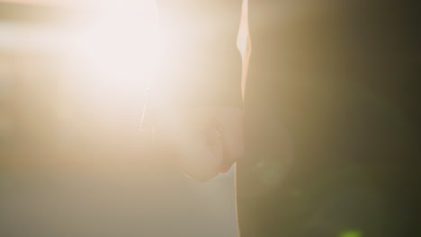 close-up of hand in black sleeve softly illuminated by golden sunlight, showing relaxed yet intentional posture, warm, blurred background highlights urban setting with reflective light