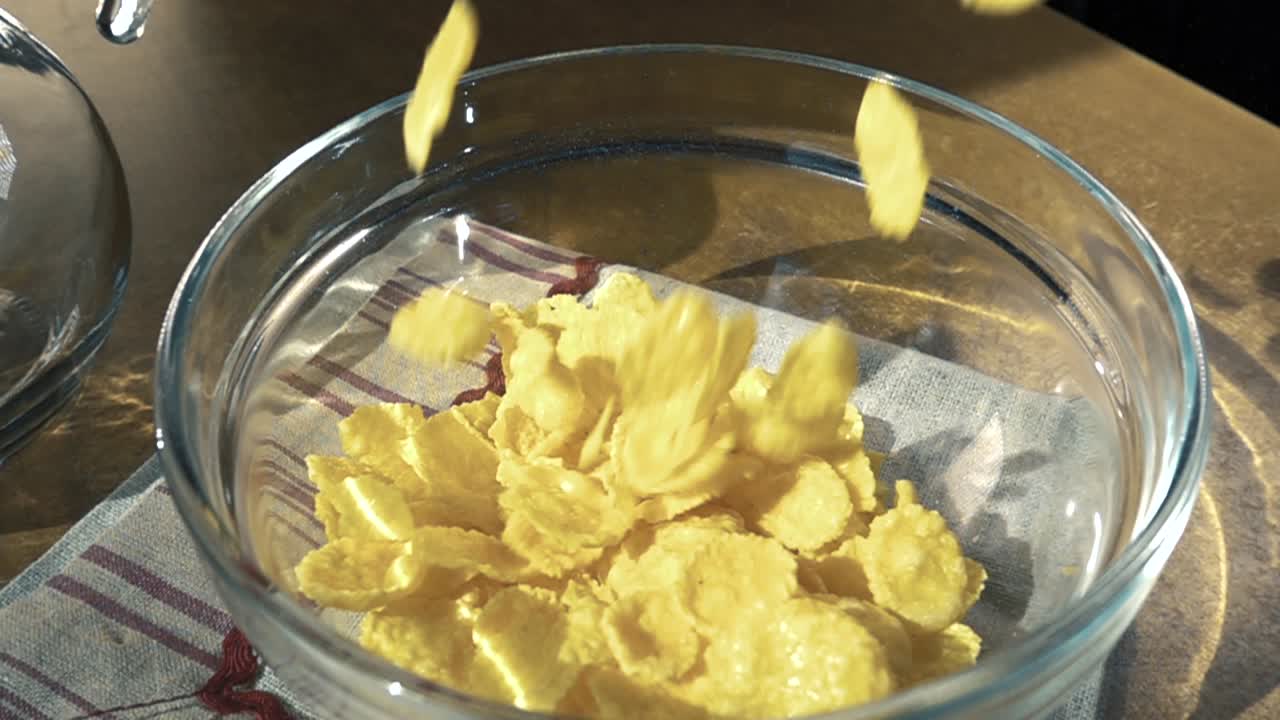 Crispy yellow corn flakes into the bowl for the morning a delicious Breakfast with milk. Slow motion with rotation tracking shot.