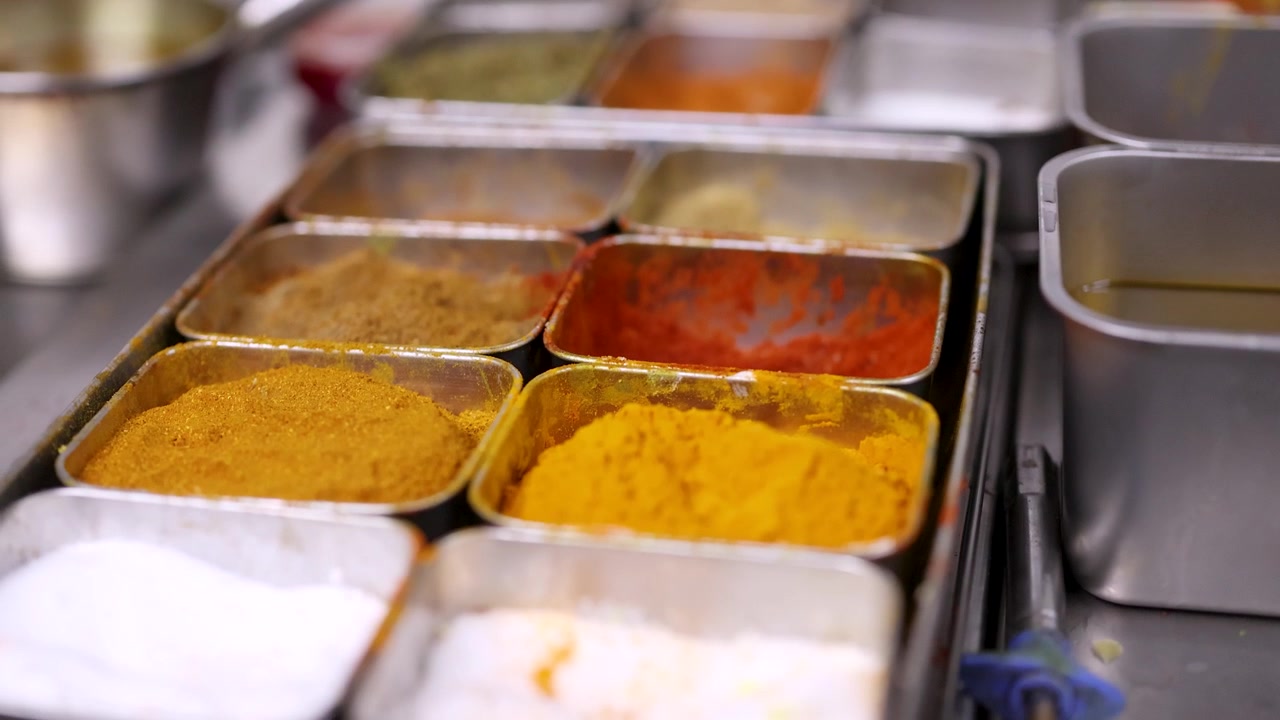 Close-up shot of various ground spices and herbs arranged in stainless steel kitchen containers.