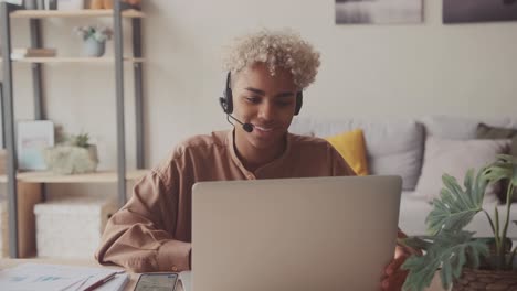 dark skinned female wears headset conference video calling in home office