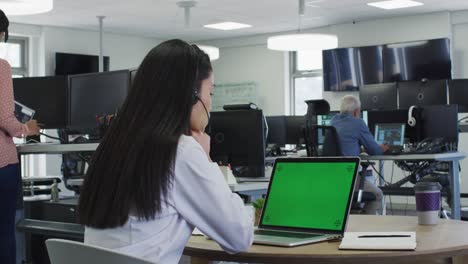vista trasera de una mujer con auriculares hablando mientras estaba sentada en su escritorio en la oficina