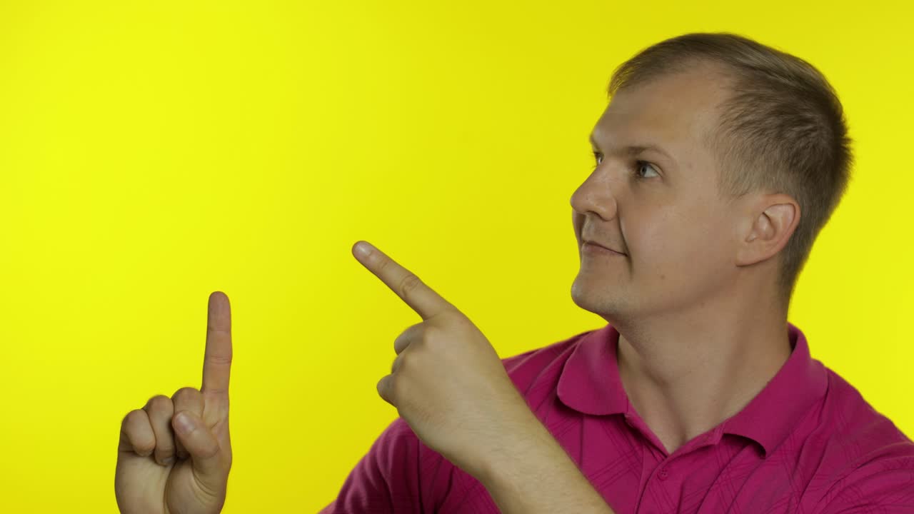 Portrait of young man posing in pink t-shirt. Happy smiling guy pointing at something with hand