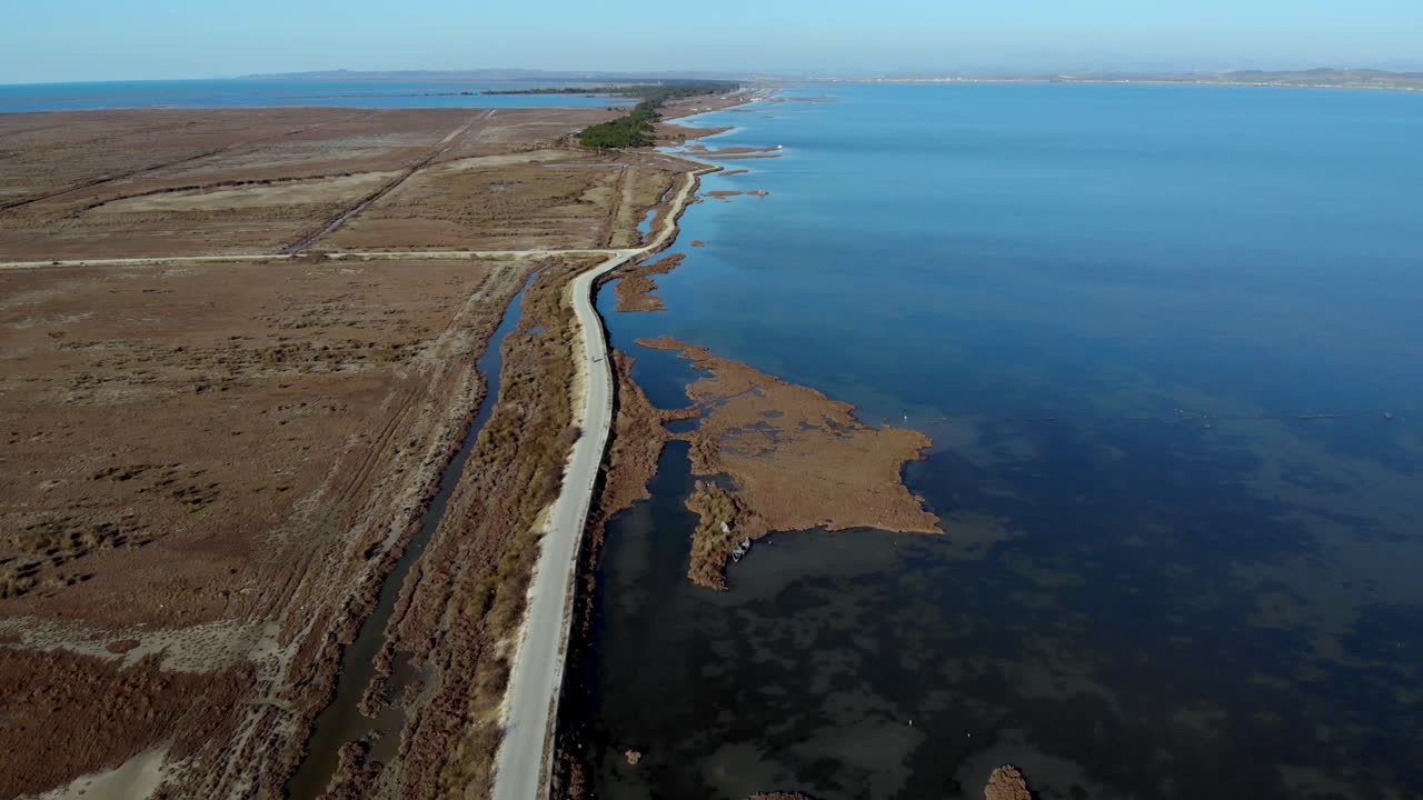 Road dividing beautiful lagoon with calm shallow water, from swamp with reeds and brown grassland, aerial view
