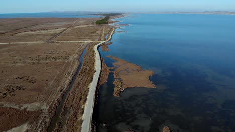 road dividing beautiful lagoon with calm shallow water, from swamp with reeds and brown grassland, aerial view