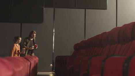 pareja entrando a un cine y encontrando asientos usando la linterna del teléfono antes de que comience la película 2