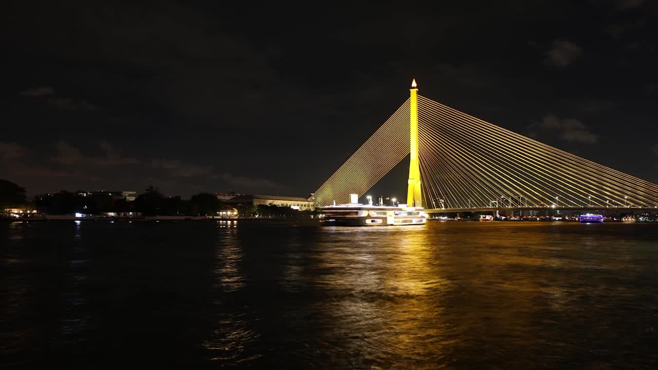 Night lapse of Rama VIII Bridge and Chao Phraya River with ferries passing by, Bangkok