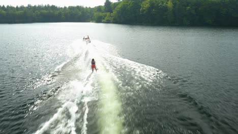 outdoor shot of a woman water skiing outside in a blue lake with many luscious, green trees in the background and a cloudy sky, a splash of water or waves can be observed