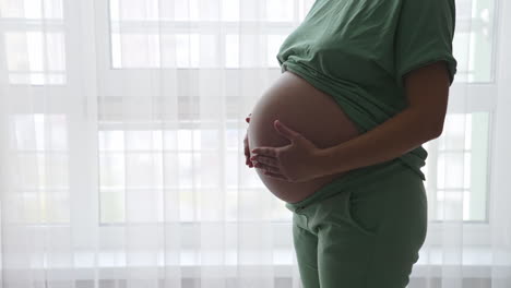 pregnant woman standing near the window and relaxing at home. maternity prenatal care and woman pregnancy concept