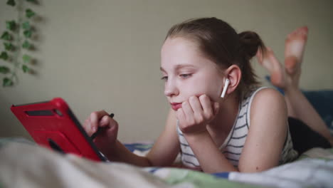 teenage girl lying on bed using tablet